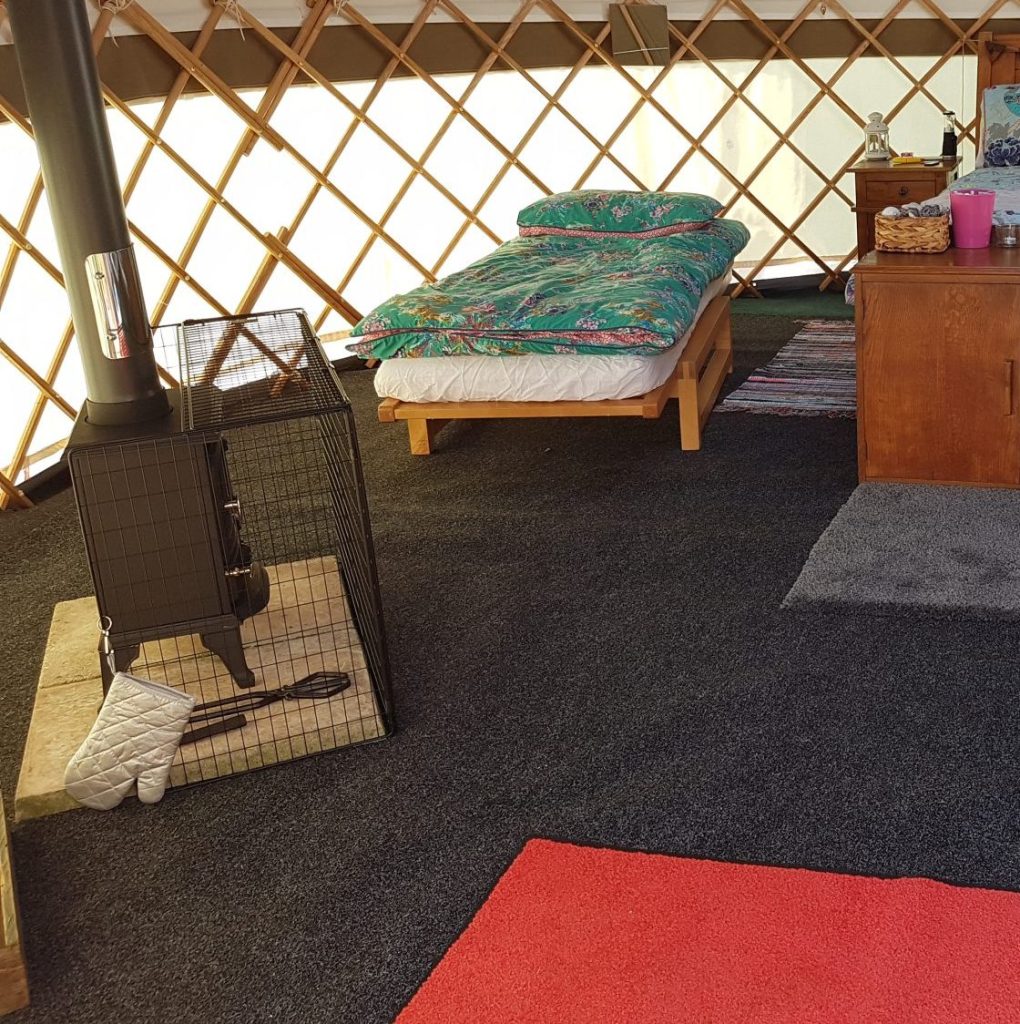 A cozy bedroom inside a yurt, featuring a bed, warm textiles, and natural light filtering through the circular top.