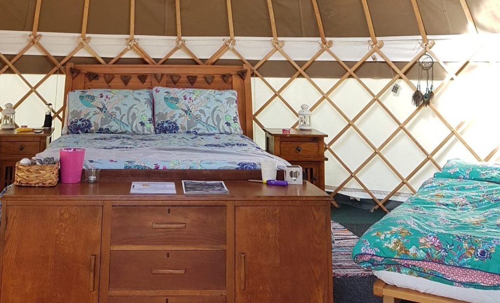 A cozy bed inside a yurt featuring a distinctive circular roof, showcasing a unique and inviting sleeping space.