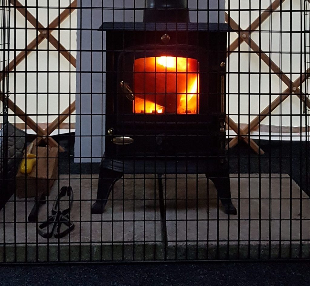 A stove with a fire burning inside, located within a cozy yurt setting.